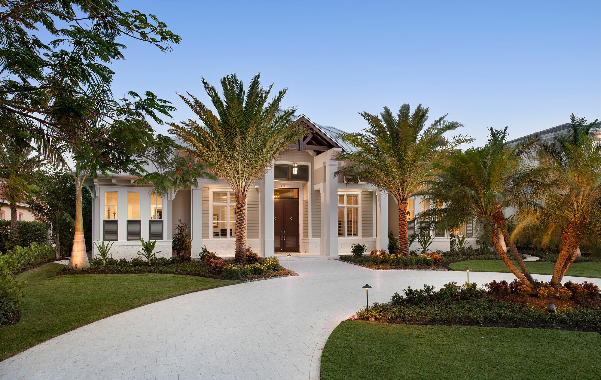 Elegant modern home with palm trees and a curved driveway at dusk.